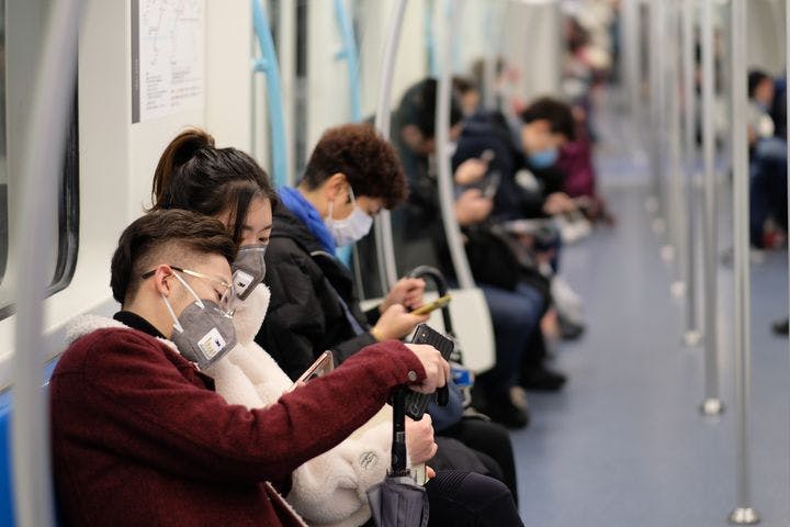 People sitting on a subway train with masks on.