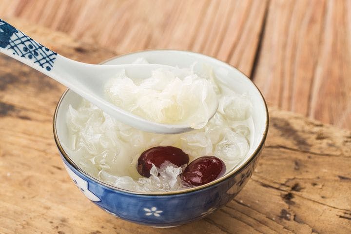 A dessert prepared using white fungus and dates in a ceramic bowl placed on a wooden table 