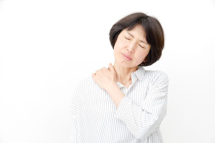 Asian woman holding her shoulder, grimacing slightly in pain