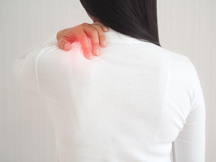 Asian woman with her back turned, touching her frozen shoulder
