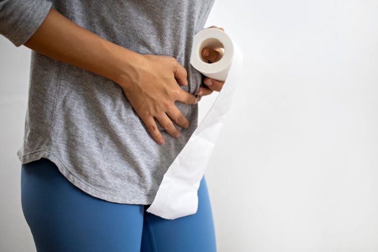 Woman holding a tissue roll with her left hand and placing her right hand on her abdomen