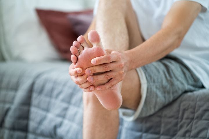 A partial view of a man holding the back of his foot in pain.