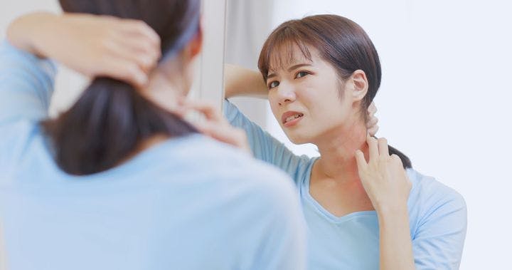 A woman checking red rashes on her neck in the mirror