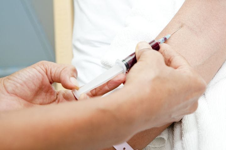 A person inserting a syringe needle to draw a patient’s blood