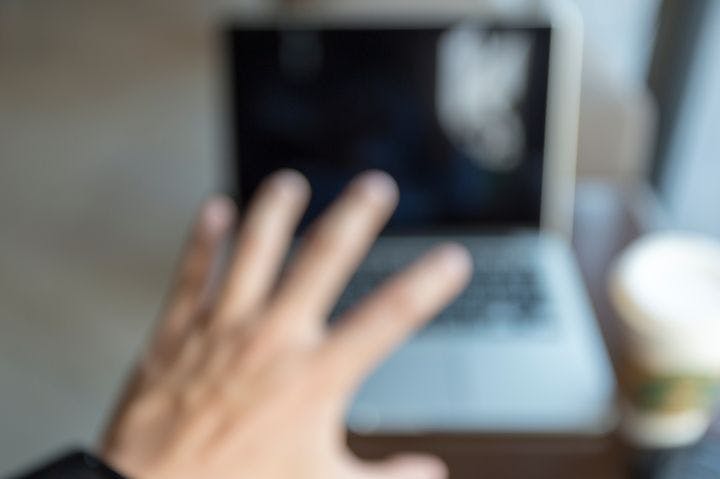 Man reaching out to touch a laptop with his left hand despite having blur vision