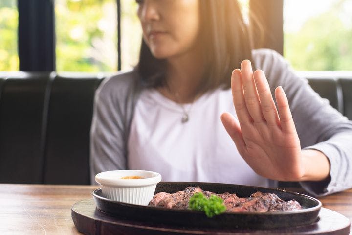 Woman lifts her hand to say no to a sizzling steak.