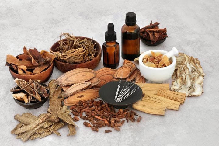 Various Chinese herbs, potions, and acupuncture needles on a light grey background
