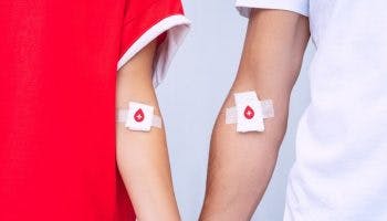 Arms of a man and woman that are bandaged with cotton pads and tapes with blood donation symbols