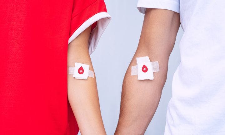 Arms of a man and woman that are bandaged with cotton pads and tapes with blood donation symbols