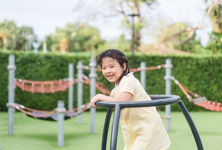 An Asian girl playing on a swing with a smile on her face