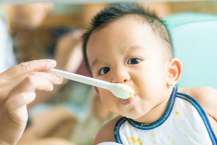 An infant wearing a bib and being spoon-fed by a caretaker