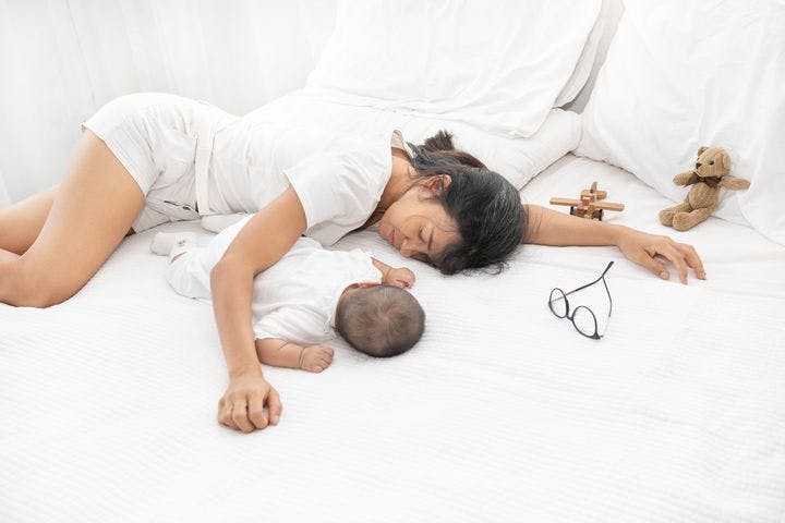 Woman sleeping in bed with her baby laying down beside her 