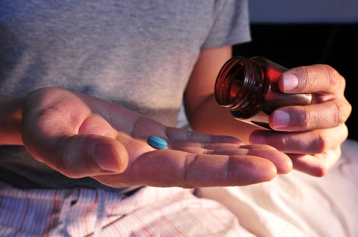 Man dropping a blue-coloured pill into his right palm while holding a medication bottle in his left