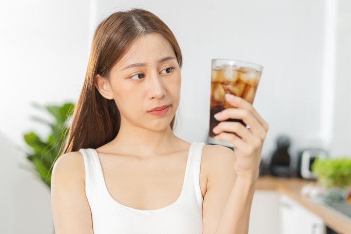 Woman looks at a glass of cold drink in her hand with a concerned expression