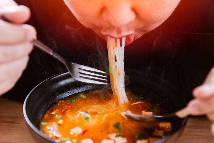 Man eating a bowl of noodles in a spicy broth