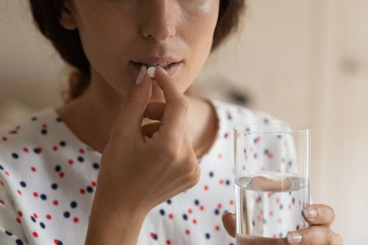 Woman taking a pill while holding a glass of water
