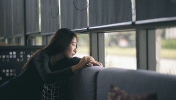 A woman sitting alone on the sofa while staring out of the window, looking contemplative.