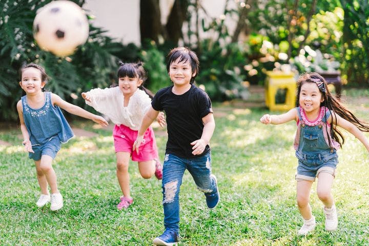 Four young children chasing a football outdoors.