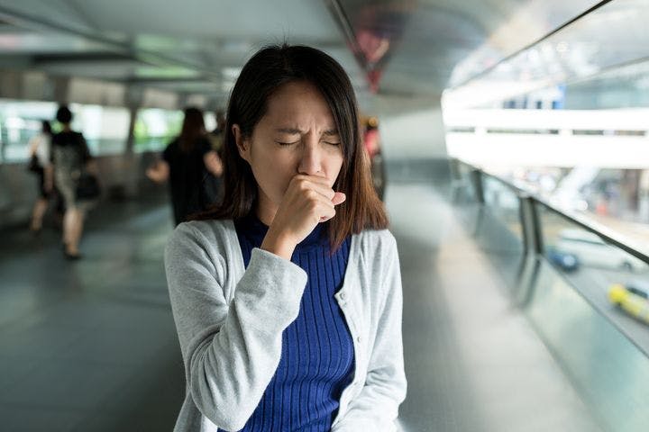 Woman coughing while standing on an overhead bridge