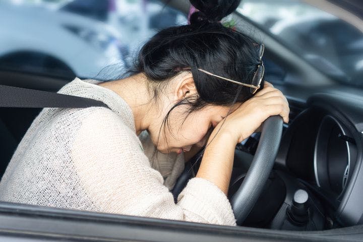 Tired woman rests her head on the steering wheel of her car. 