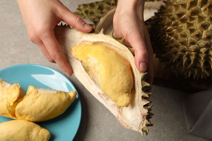 Woman holding a durian shell that’s holding a single pulp