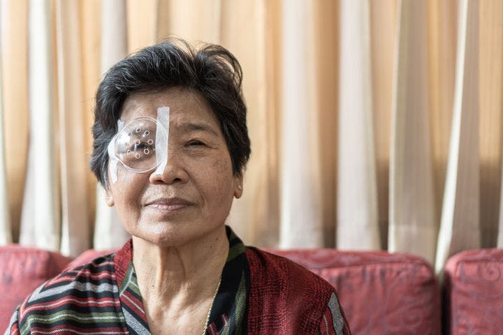 Close-up of an elderly woman sitting on a sofa with a plastic cover taped over right eye 