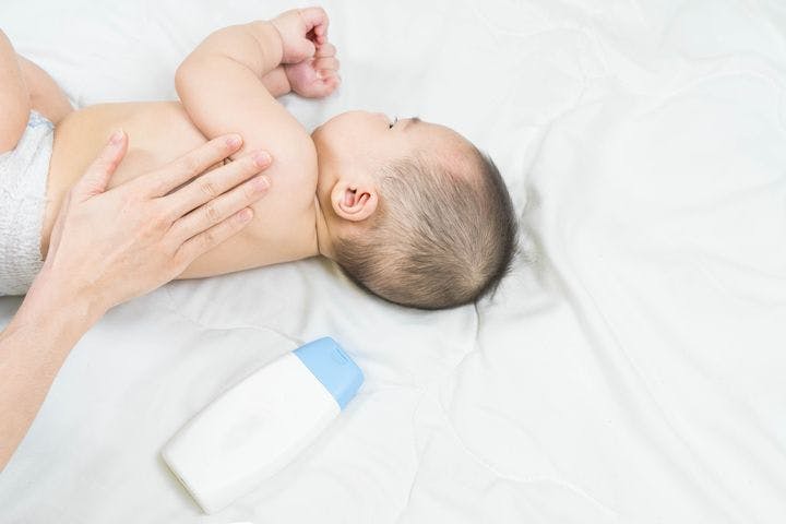 A baby on the bed with the parent rubbing lotion on the baby’s skin