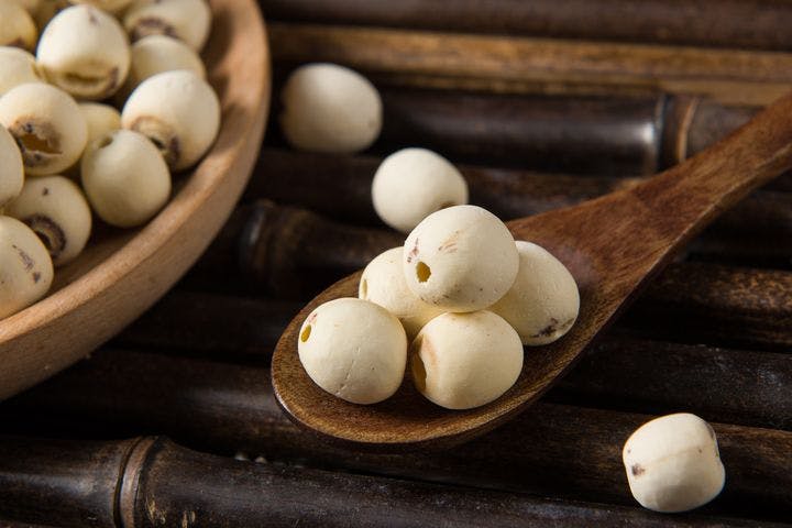 Dried lotus seeds on a wooden spoon and in a wooden bowl on a bamboo table.
