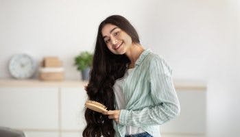 Young Indian lady brushing her wavy long hair, using wooden brush indoors 