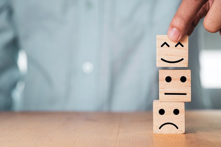 Man using his fingers to place a wooden block with a happy face on top of two other blocks with faces