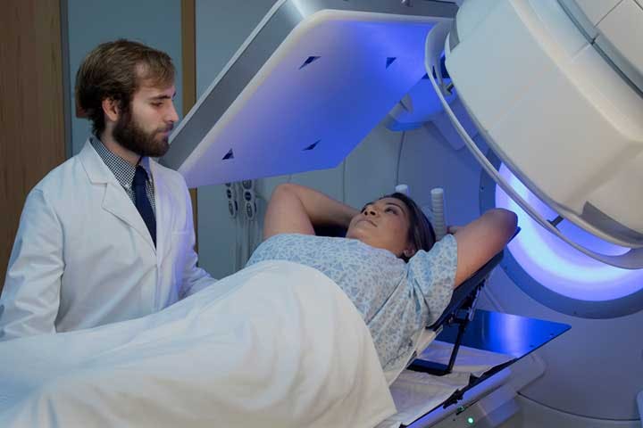 Woman lying on her back with her hands behind her head as she talks to a physician before radiation therapy