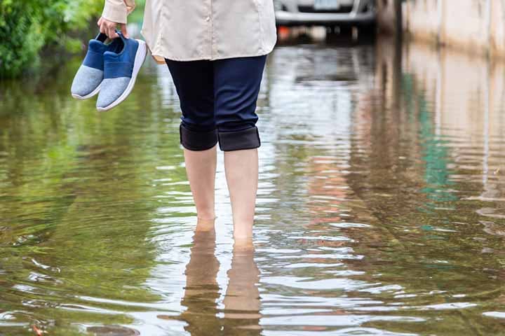 Woman wading through water with shoes in her hands. 