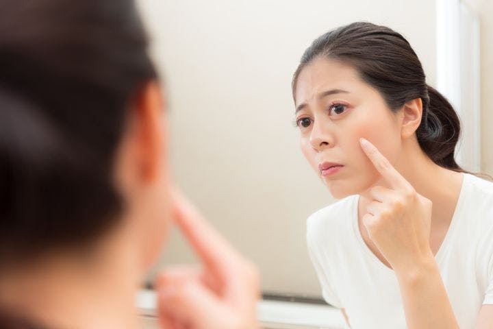 Photo of a young woman looking into the mirror with a finger on her cheek