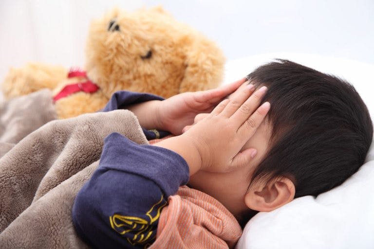 Little boy covering his face in embarrassment while lying in bed