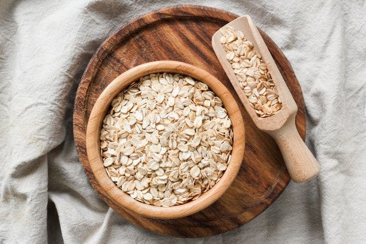 Rolled oat flakes inside a wooden bowl and spoon