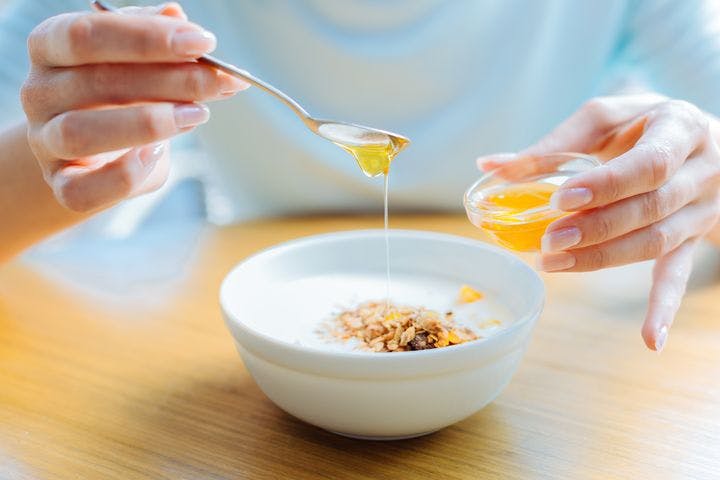 A person drizzling honey on a bowl of cooked oats