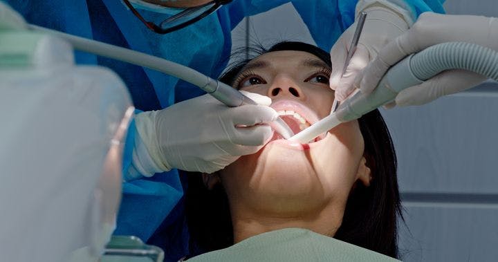 A close-up of a woman lying down while being examined by a dentist with tubes in her mouth.
