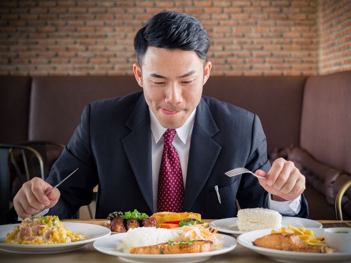 An Asian man in a suit eating five plates of food in a restaurant