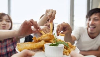 A group of people taking french fries from a plate of fish and chips