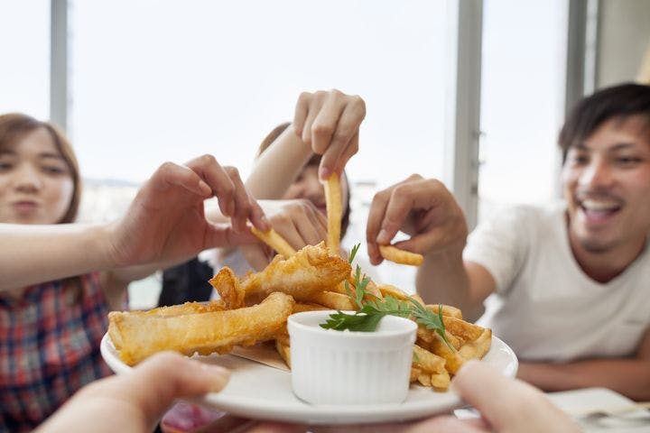 A group of people taking french fries from a plate of fish and chips