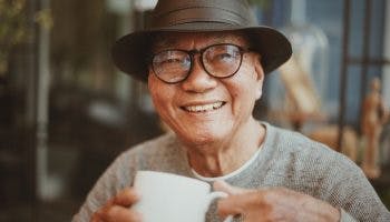 Older man smiling as he holds a white cup of coffee with both hands
