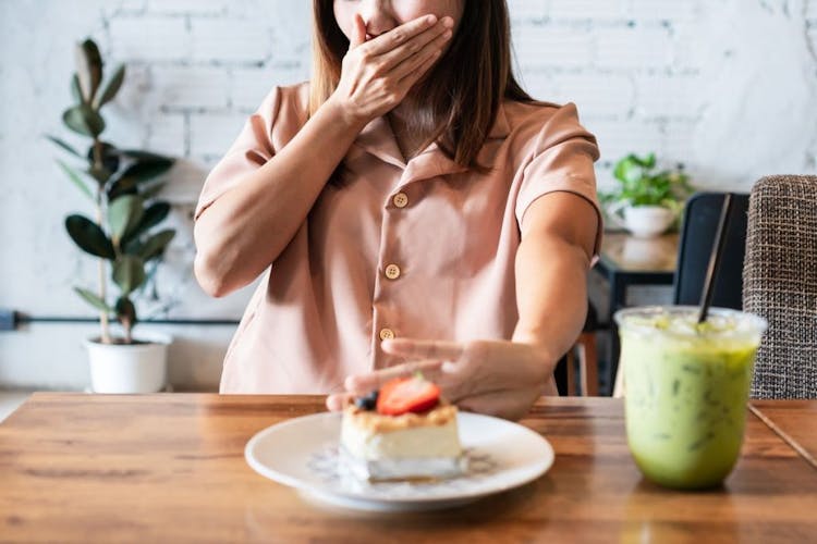 A woman covering her mouth and pushing off a plate of cake In front of her