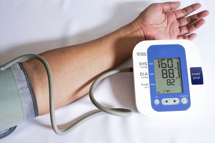 Person’s hand in a cuff belt that’s connected to a blood pressure monitor with a reading of 160/88