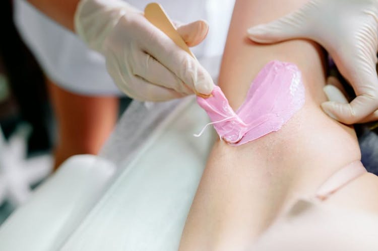 Hands of salon worker applying pink-coloured wax to armpit for hair removal