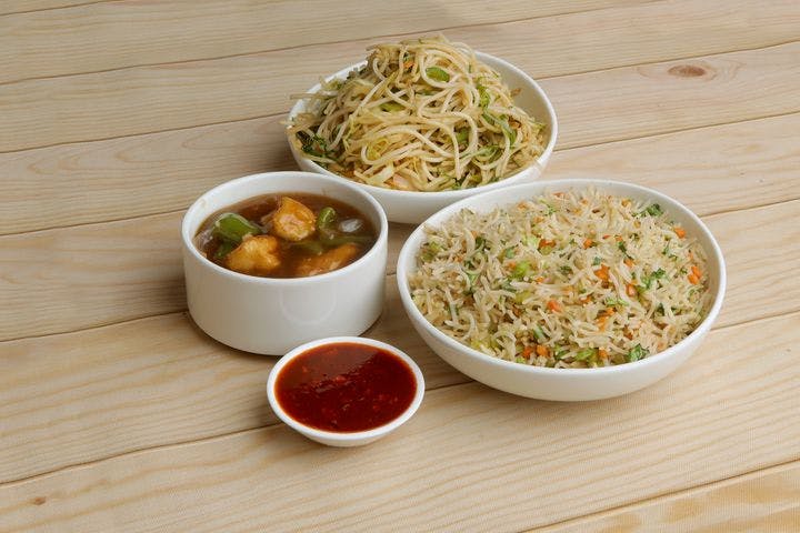 A bowl of noodles served with a portion of rice, a small plate of chilli sauce, and a bowl of soup