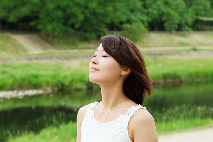 Woman breathing in the air outdoors surrounded by greenery, demonstrating nose breathing vs mouth breathing
