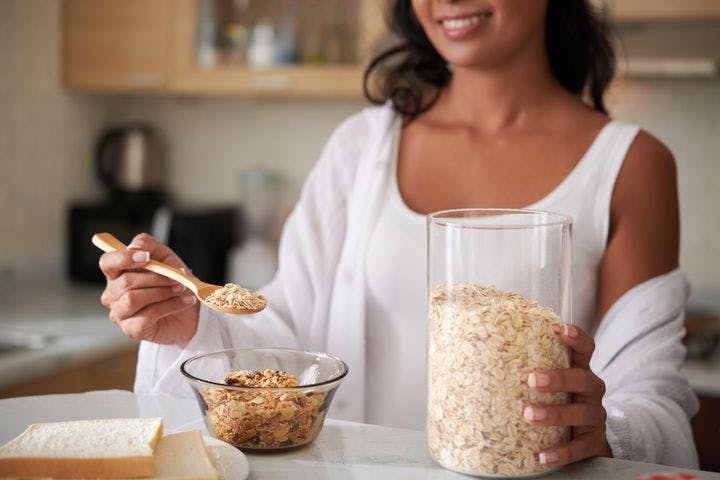 A woman adding a spoon of oat flakes to a clear bowl