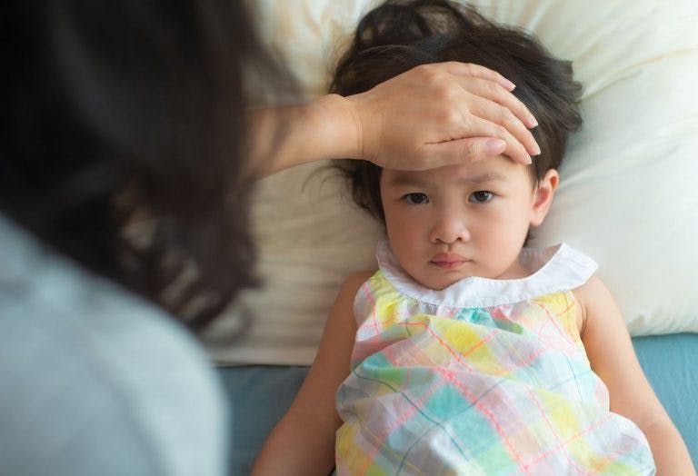 A mother checks a feverish toddler’s forehead.