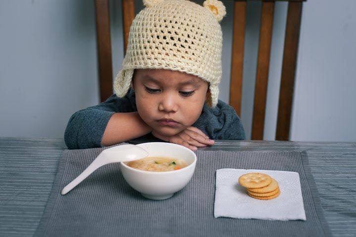 Little boy looking tired, sitting in front of a bowl of light soup and crackers.