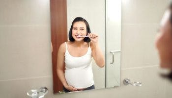 A pregnant woman standing in front of a bathroom mirror while brushing her teeth.